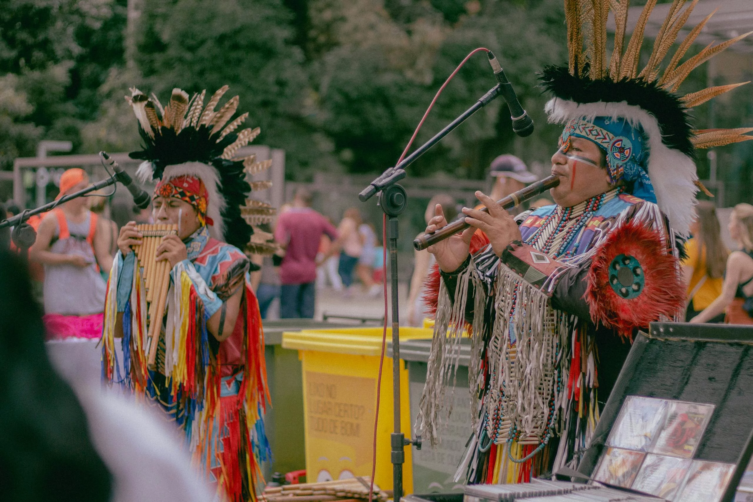 Native American musicians performing outdoors in traditional wear with woodwind instruments